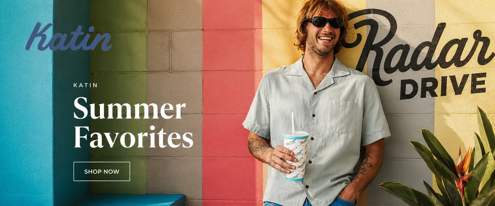 Man holding a drink in front of a colorful wall with 'Katin' and 'Radar Drive' branding.