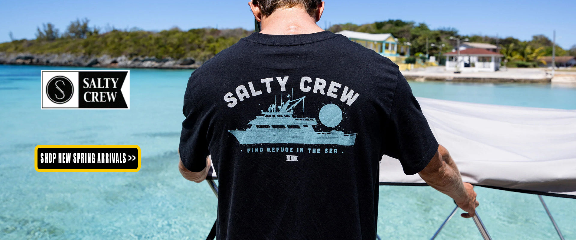 Person wearing a Salty Crew t-shirt holding a surfboard on a beach with Salty Crew branding.
